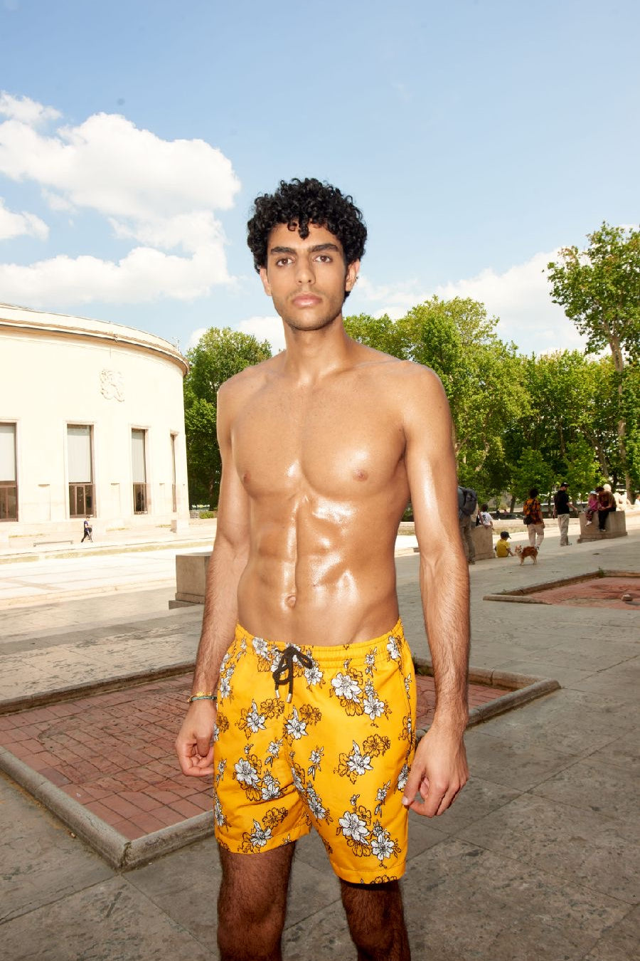 Photo d'un homme portant le short de bain jaune à fleur blanche. Il est torse nu et se tient de debout.