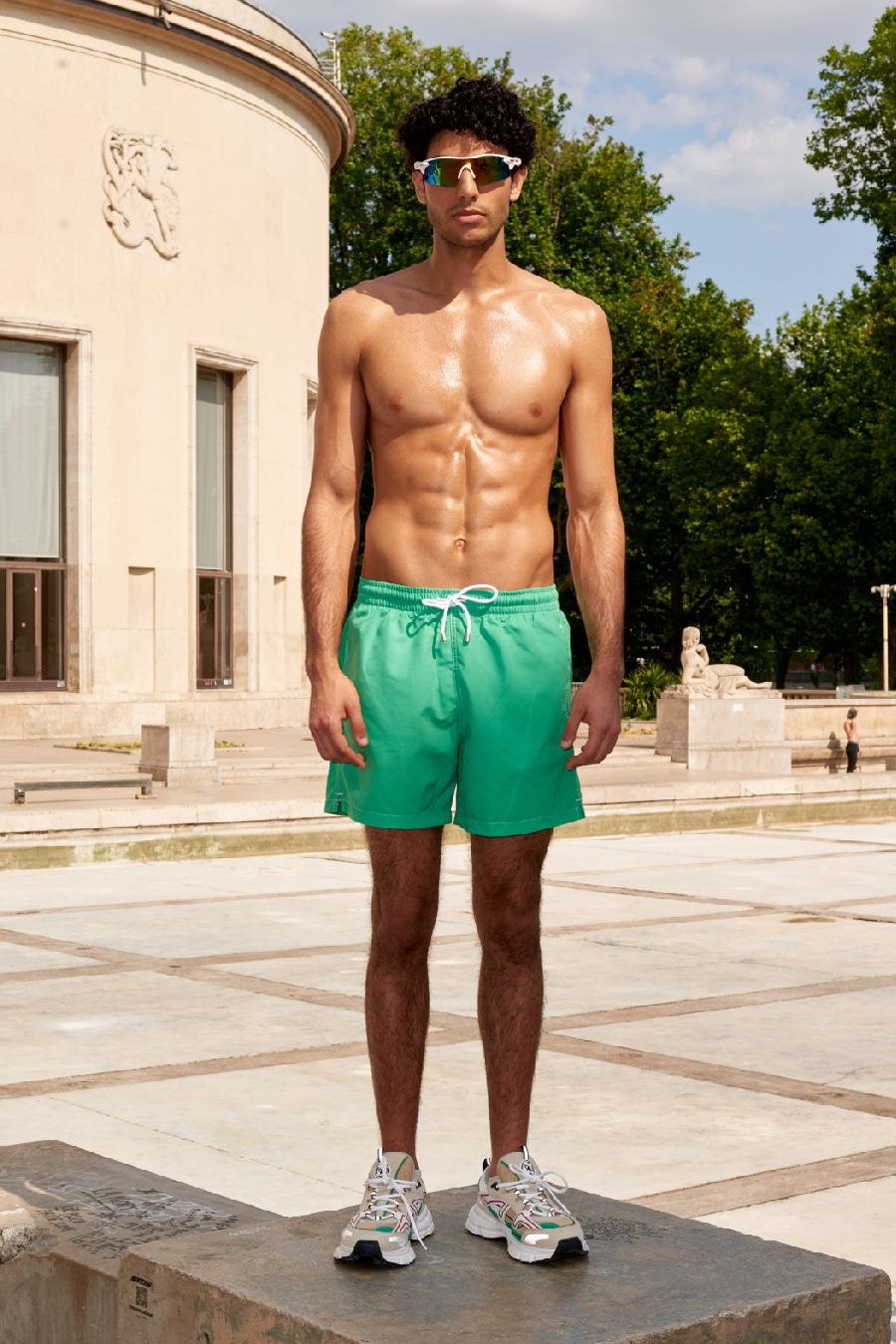 Photo d'un homme portant le short de bain vert matcha. Il est torse nu et se tient de debout.