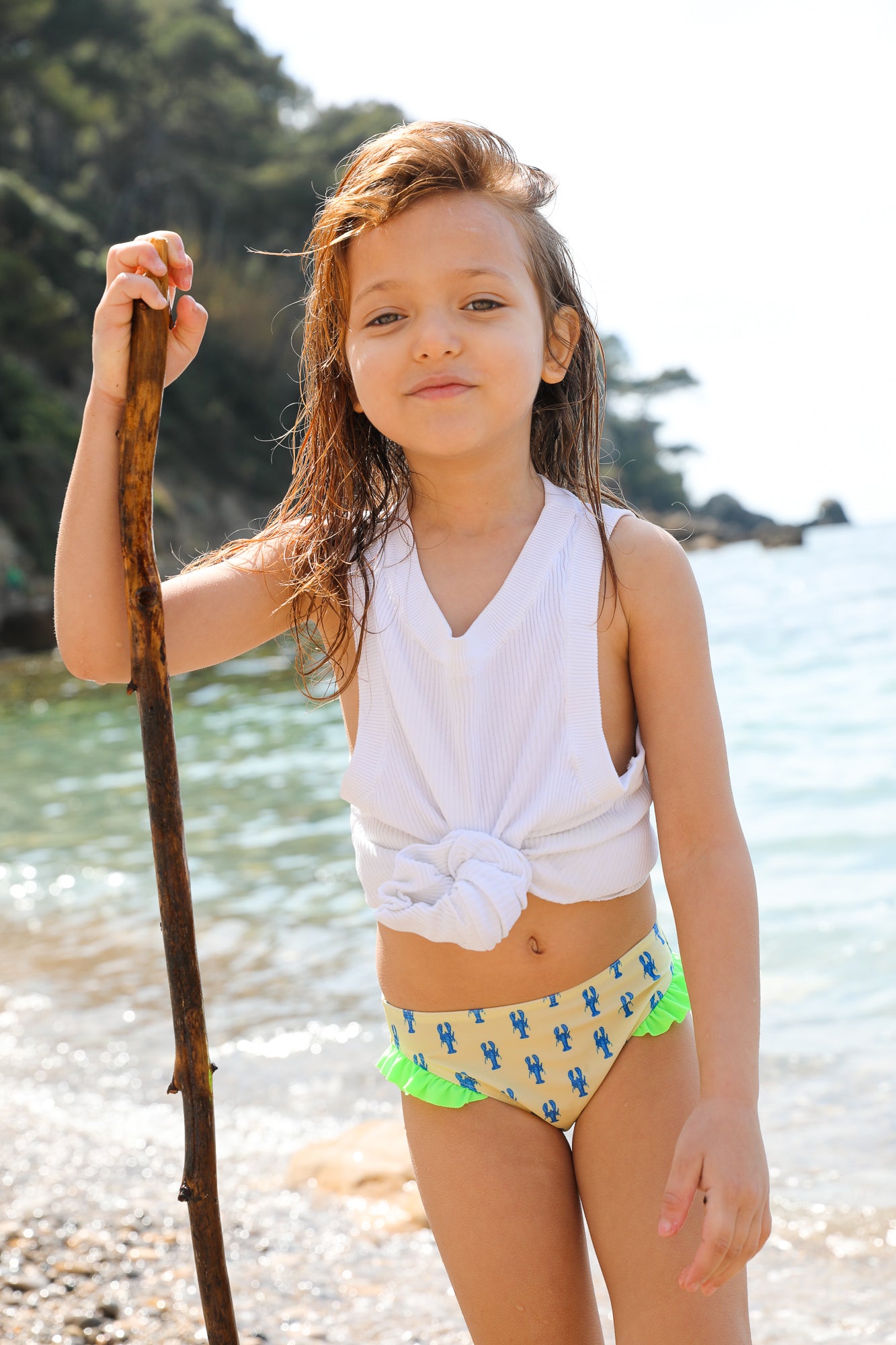 Photo d'une petite fille à la mer portant la culotte de maillot de bain Lolo avec des homards bleus et des froufrous verts sur les côtés