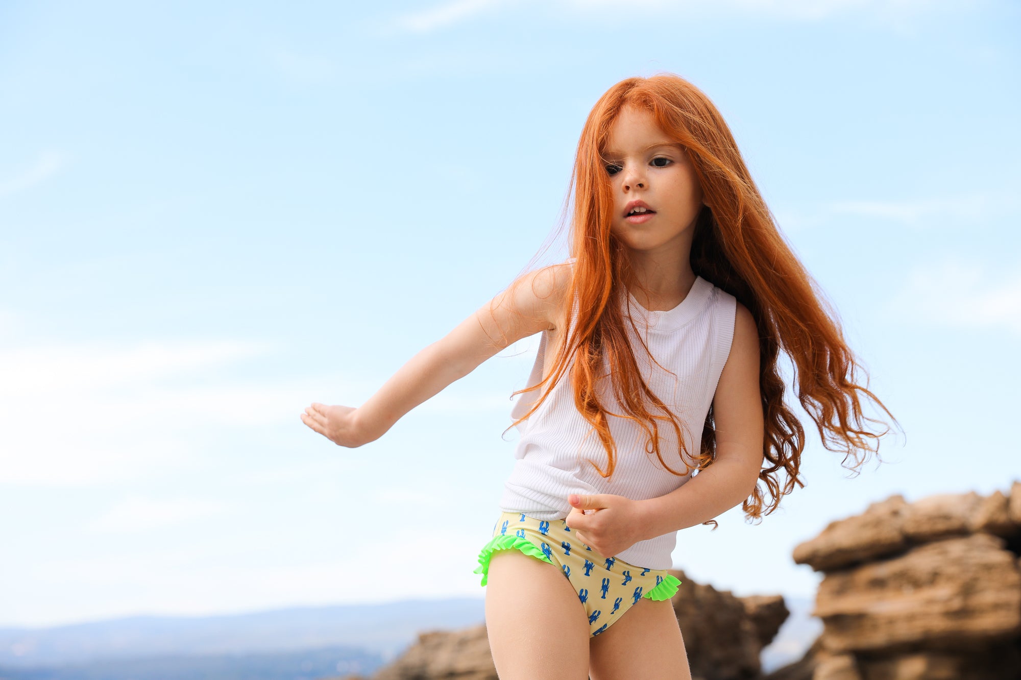 Photo d'une petite fille à la mer portant la culotte de maillot de bain Lolo avec des homards bleus et des froufrous verts sur les côtés