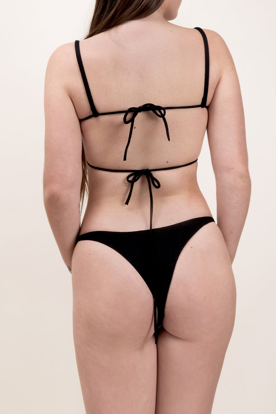 Photo d'une femme de dos portant le bas de maillot de bain Tanga en noir.