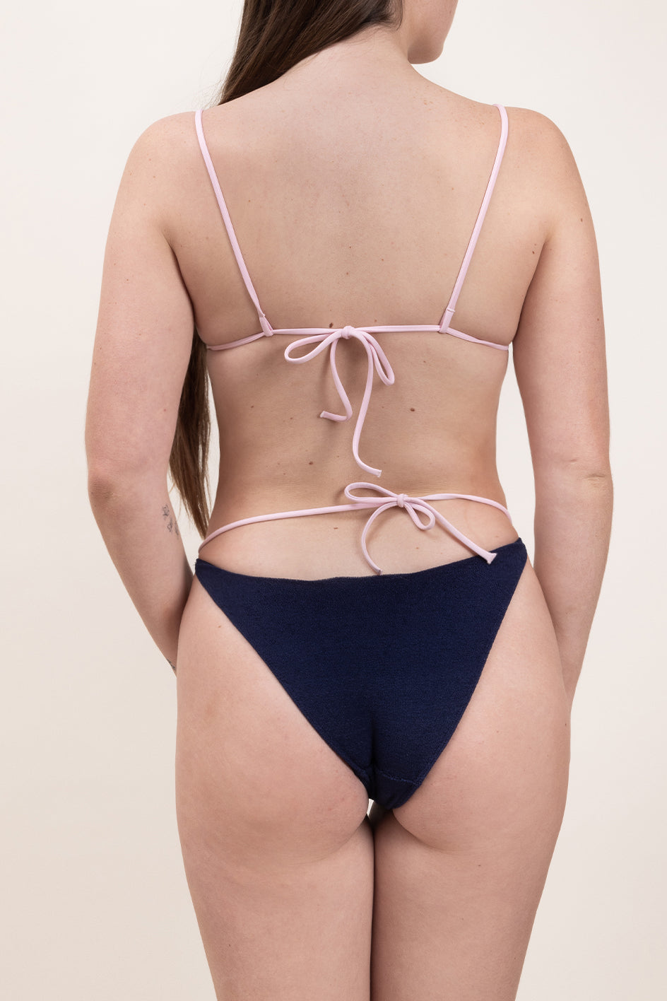 Photo d'une femme de dos portant le bas de maillot de bain Tiana en matière éponge bleu marine à bretelles rose claire