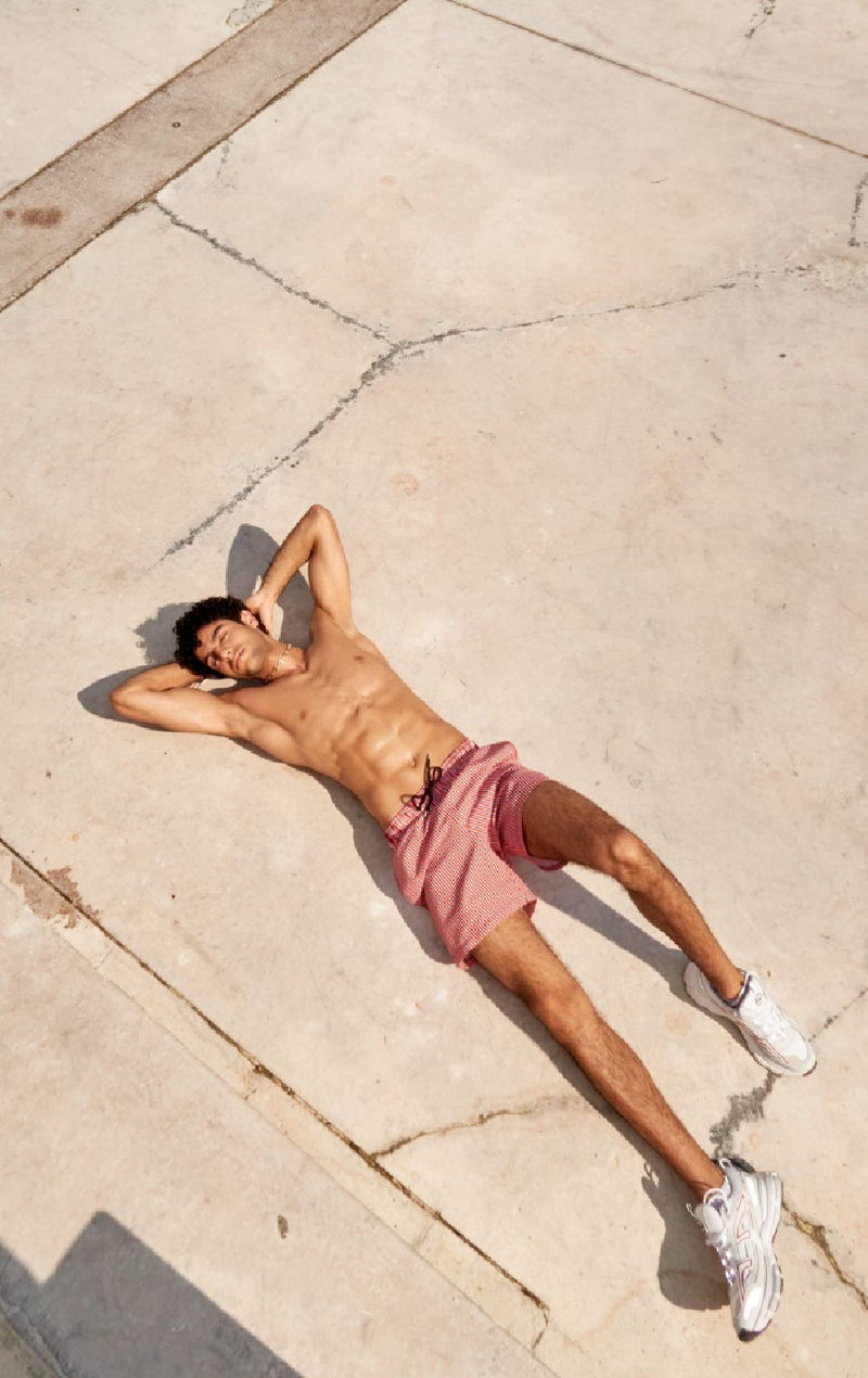 Photo d'un homme portant le short de bain rouge rayé. Il est torse nu et se tient allongé.