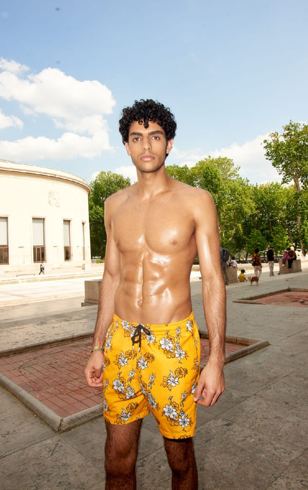 Photo d'un homme portant le short de bain jaune à fleur blanche. Il est torse nu et se tient de debout.