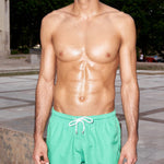 Photo d'un homme portant le short de bain vert matcha. Il est torse nu et se tient de debout.
