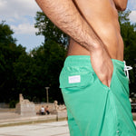 Photo rapprochée du short de bain, où on aperçoit la poche arrière avec le logo POOLDAY en violet. 2 poches à l'avant et un cordon blanc à la taille