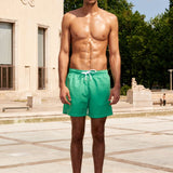 Photo d'un homme portant le short de bain vert matcha. Il est torse nu et se tient de debout.