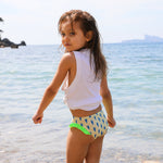 Photo d'une petite fille à la mer de dos portant la culotte de maillot de bain Lolo avec des homards bleus et des froufrous verts sur les côtés