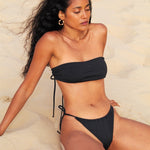 Photo d'une mannequin assise à la plage portant le haut de maillot de bain Batroun noir