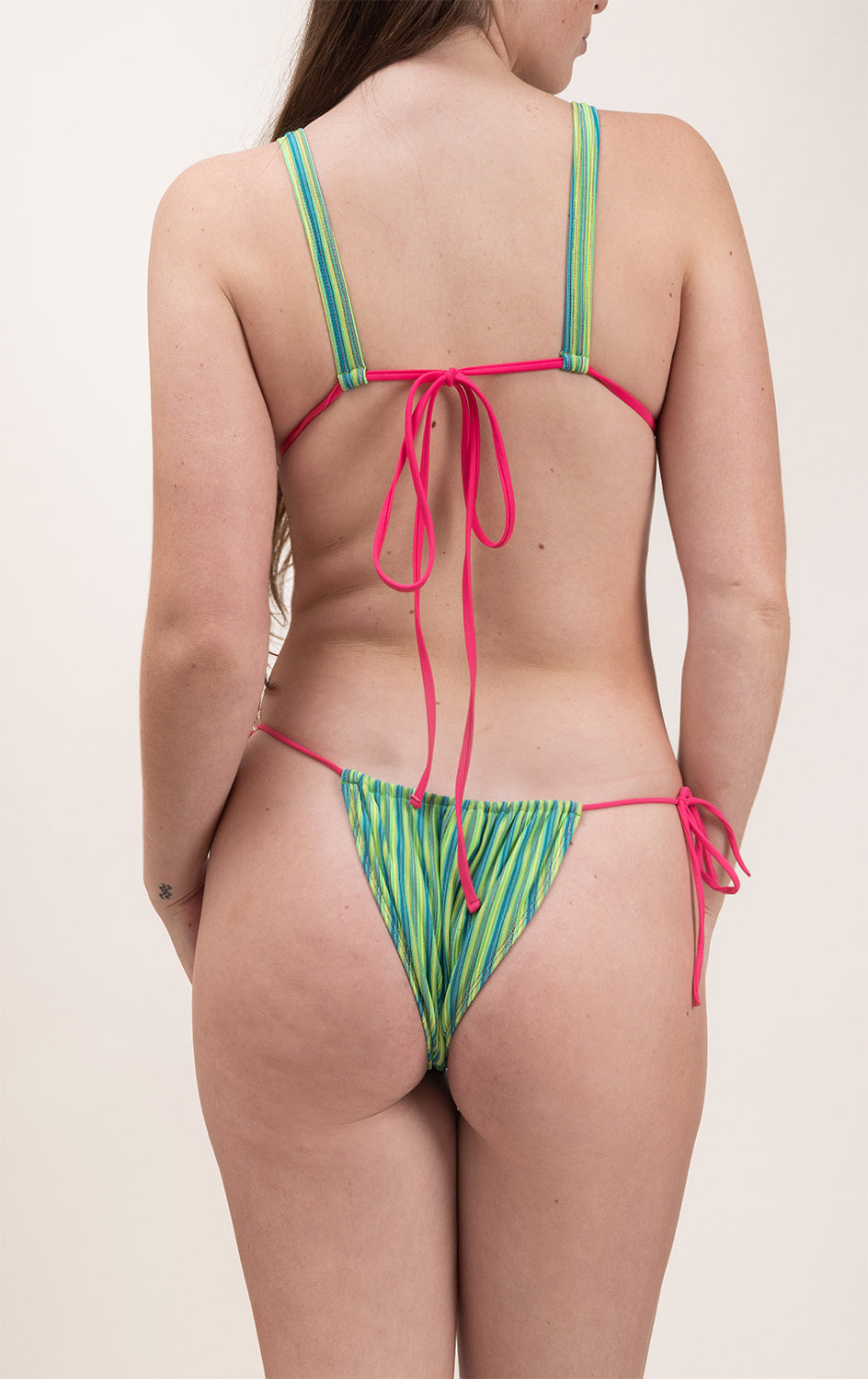 Photo de dos d'une femme portant le maillot de bain Alaior vert rayé avec les ficelles de couleur rose fuschia
