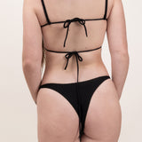 Photo de dos d'une femme portant le bas de maillot de bain Tanga en noir jacquard.