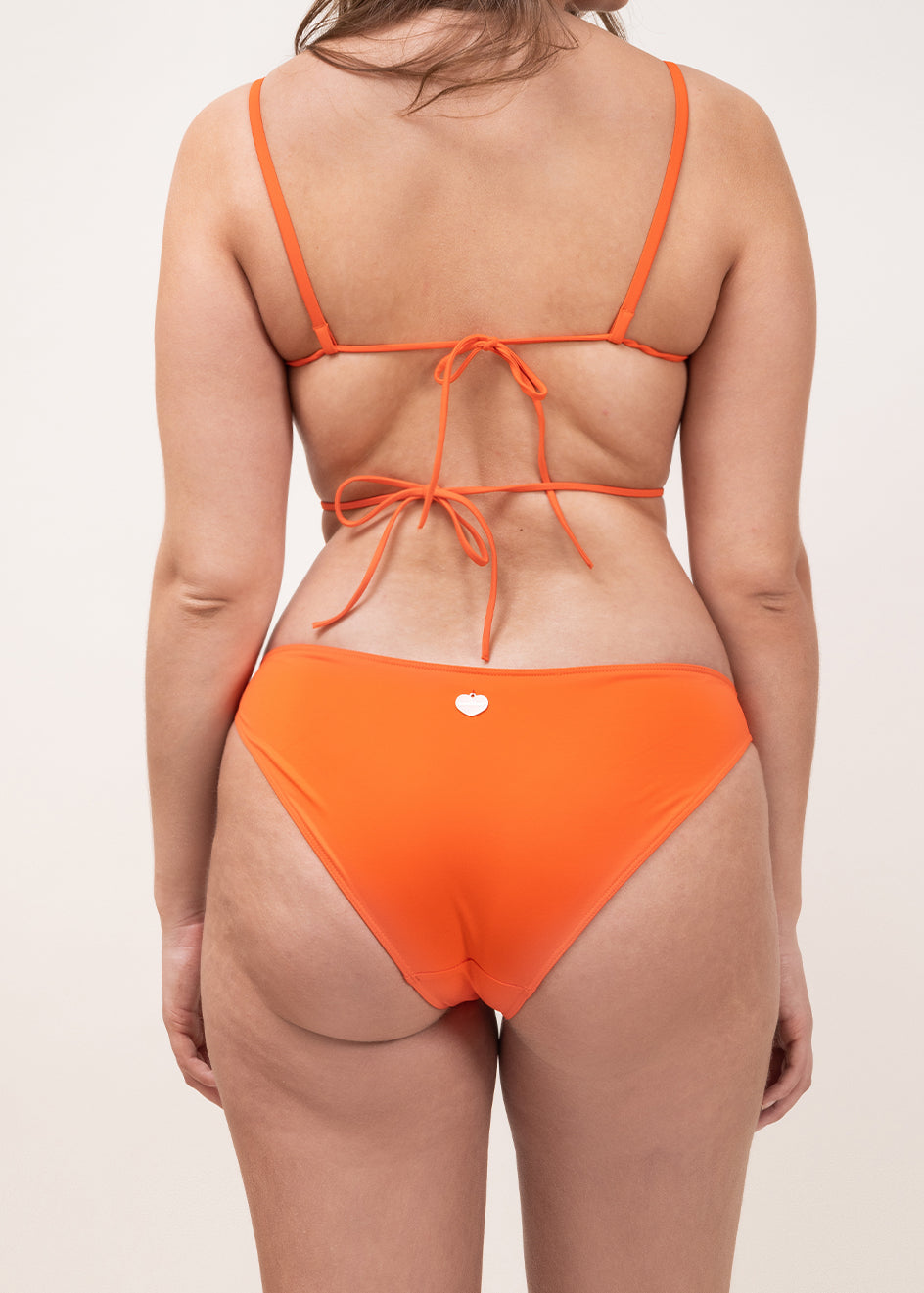 Photo d'une femme à forte poitrine de dos portant le haut de maillot de bain Ponza en orange