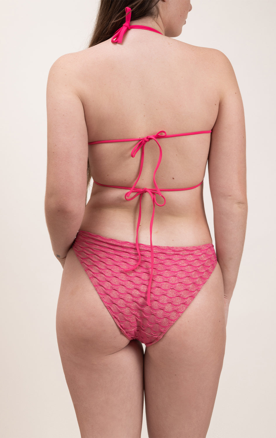 Photo d'une femme de dos portant le haut de maillot de bain Ponza en fuschia/lurex