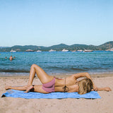 Photo d'une mannequin allongée de côté au bord de la mer, portant le maillot de bain une pièce Donatella rouge rayé
