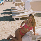 Photo d'une femme blonde assise sur un transat à la plage portant le maillot de bain Bari rose fuschia