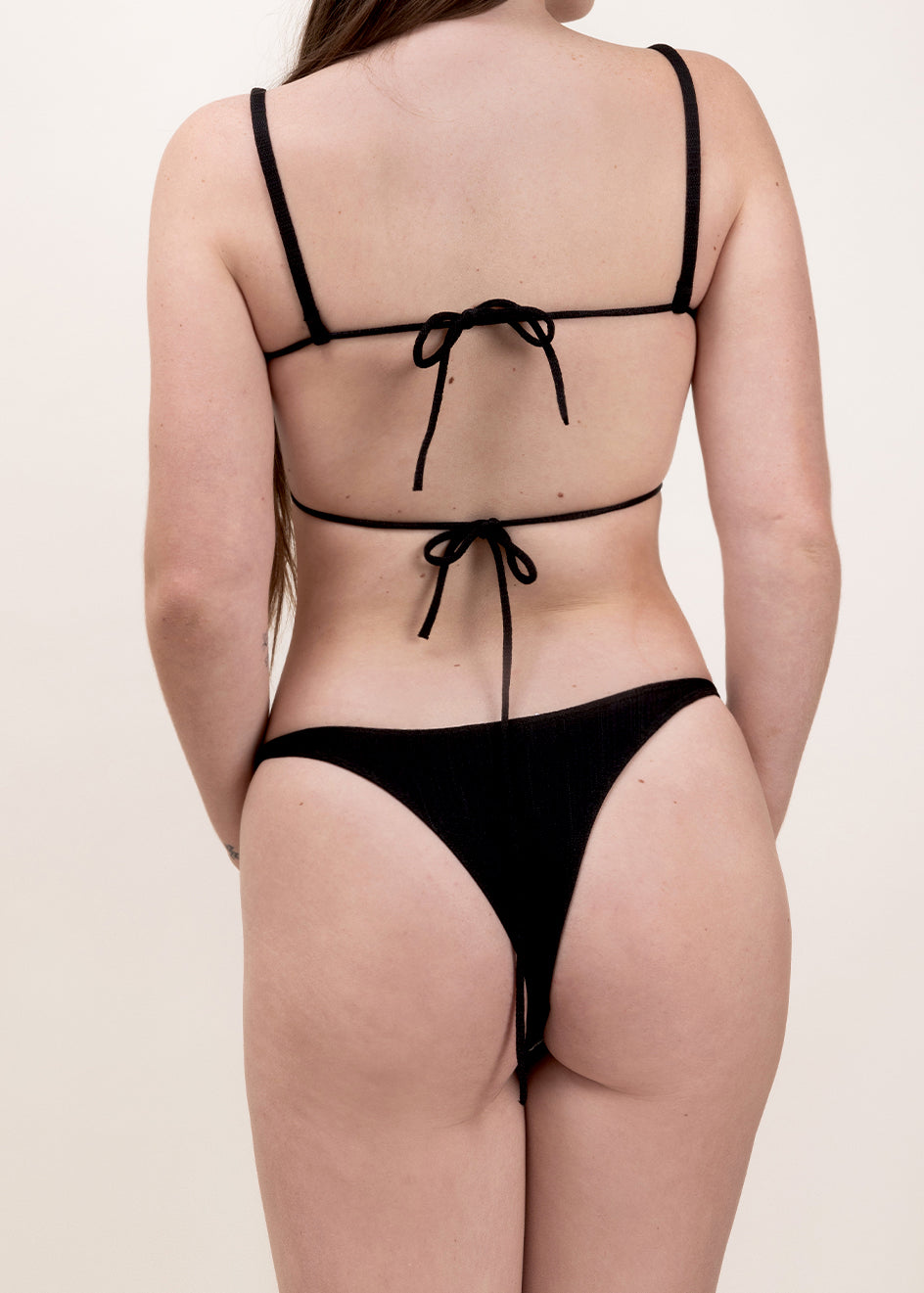 Photo d'une femme de dos portant le bas de maillot de bain Tanga en noir.