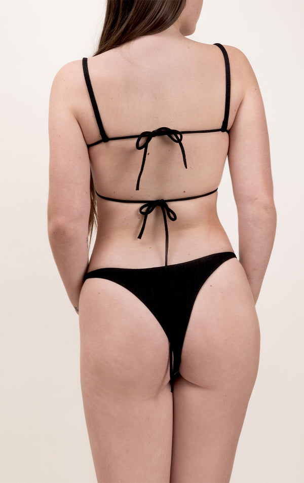 Photo d'une femme de dos portant le bas de maillot de bain Tanga en noir.
