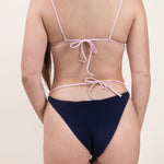 Photo d'une femme de dos portant le bas de maillot de bain Tiana en matière éponge bleu marine à bretelles rose claire