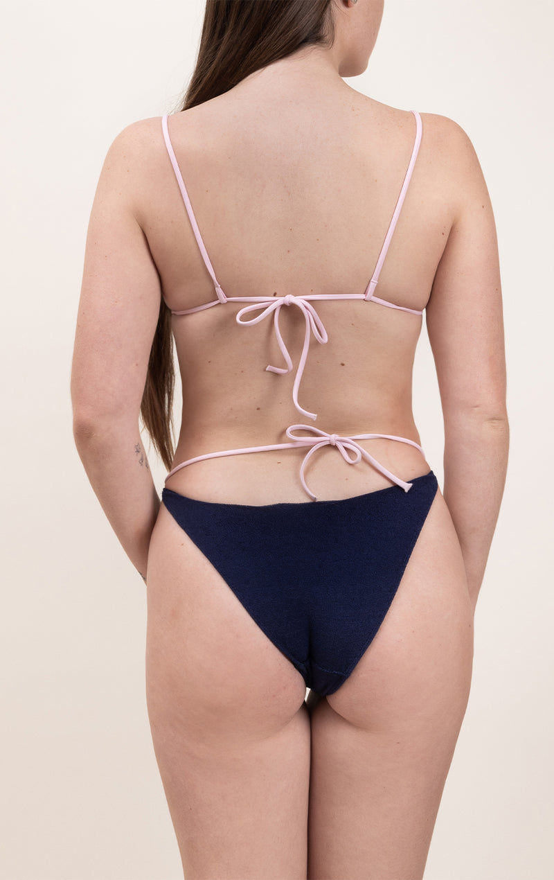 Photo d'une femme de dos portant le bas de maillot de bain Tiana en matière éponge bleu marine à bretelles rose claire